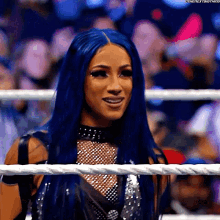 a woman with long blue hair is standing in a wrestling ring .