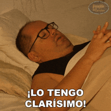 a man with glasses is laying in bed with the words lo tengo clarisimo