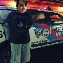 a young boy is standing in front of a police car wearing a hogwarts shirt .