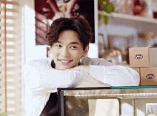 a young man is leaning on a counter and smiling while wearing an apron .