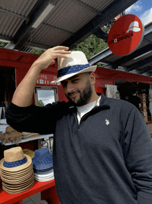 a man wearing a hat stands in front of a red sign that says tete de chapeaux