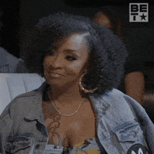 a woman wearing a denim jacket and hoop earrings is sitting in front of a be t logo