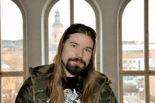 a man with long hair and a beard is in front of a window .