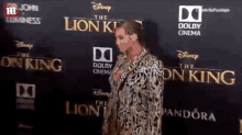 a woman is standing on a red carpet in front of a lion king poster .