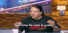 a man in a black shirt is sitting at a table and talking in arabic