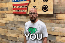 a man stands in front of a wooden wall with a sign that says we love our vets every day