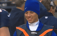 a man wearing a blue beanie and a vest that says gliman