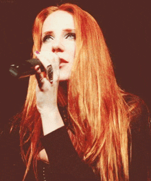 a woman with red hair singing into a microphone with a ring on her finger