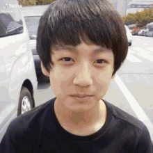 a young boy with short hair is standing in a parking lot with a white van in the background .