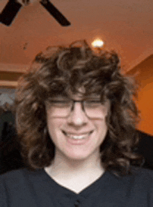 a young man with curly hair and glasses is smiling in a living room .