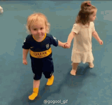 a boy wearing a qatar airways jersey holds hands with a little girl