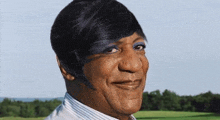 a man with a wig on his head is smiling in front of a field