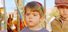 two young boys are standing next to each other at a carnival . one of the boys is wearing a red hat .