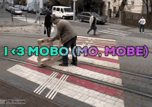 a man is pushing a wooden box across a crosswalk with the words i < 3 mobo mo mobe written on it