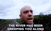 a man standing next to train tracks with the words " the river has been sweeping you along " below him