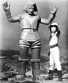 a black and white photo of a boy standing next to a large robot