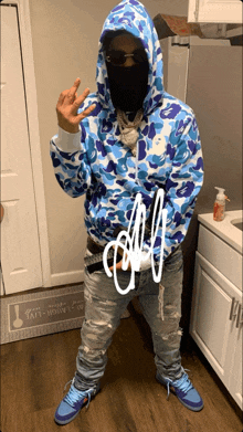 a man wearing a blue camo hoodie stands in front of a kitchen counter