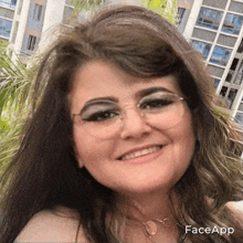 a woman wearing glasses and a necklace is smiling in front of a building with faceapp written on the bottom