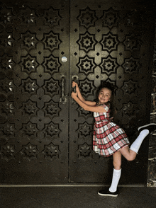 a young girl in a plaid dress stands in front of a door