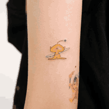 a small tattoo on a person 's arm shows a yellow alien with a ring around his head