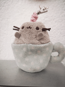 a stuffed cat in a teacup with a pink swirl on its head