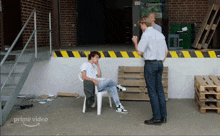 a man sits in a white chair in front of a brick building with a sign that says prime video on it