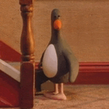 a penguin figurine is standing next to a wooden railing on a staircase .