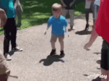 a young boy in a blue shirt is walking down a sidewalk surrounded by people and a red balloon .