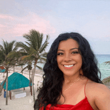 a woman in a red dress smiles in front of a beach with palm trees