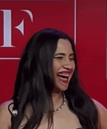 a woman with long black hair is making a funny face in front of a red wall with the letter f on it