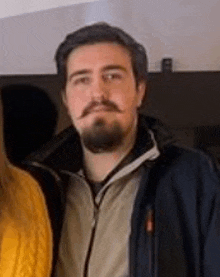 a man with a beard and mustache is posing for a picture with a woman in a yellow sweater .