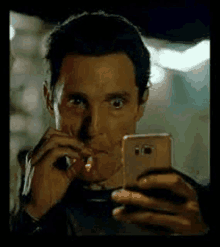 a man is smoking a cigarette while taking a selfie with his cell phone .