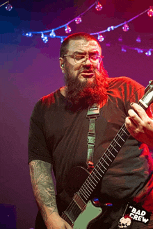 a man with a beard is playing a guitar with a bad crew sticker