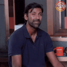 a man in a blue shirt is sitting at a table with an orange mug that says quick meal on it