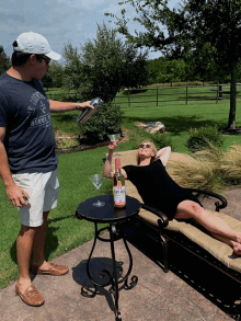 a man pouring a martini into a woman laying on a lawn chair who is holding a bottle of rose wine