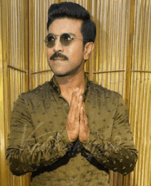 a man wearing sunglasses and a green shirt holds his hands together in prayer