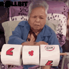 an elderly woman is sitting in a chair holding two rolls of toilet paper with wild written on them .