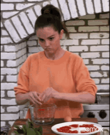 a woman in an orange sweater is preparing food in a kitchen with a plate of food in the background .