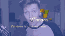 a man with a surprised look on his face is standing in front of a computer screen that says `` windows is shutting down '' .