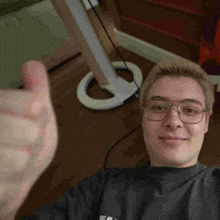 a young man wearing glasses is giving a thumbs up while taking a selfie .