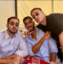 three men are posing for a picture with one wearing a tommy shirt