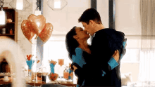 a man is holding a woman in his arms and they are kissing in front of balloons .