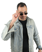 a man wearing sunglasses and a denim jacket is looking over his shoulder