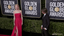 a woman in a red dress stands next to a man in a black suit on a red carpet that says golden globe