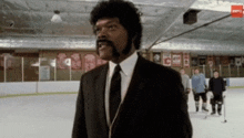 a man in a suit and tie is standing on an ice rink with hockey players in the background .