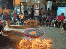 a group of people are sitting around a table with candles in the shape of the letter o on the ground