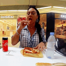 a woman sits at a table with a coca cola can and a bottle of water in front of a pandora store