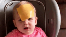 a baby with a slice of cheese on her head .