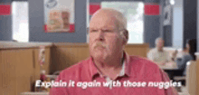 an older man in a red shirt is sitting at a table in a restaurant and talking to someone .