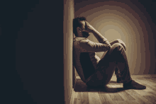 a man is sitting on the floor in a dark room with his head in his hands